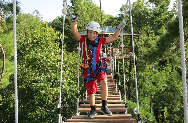 Boy walking across suspension bridge leaning forwards