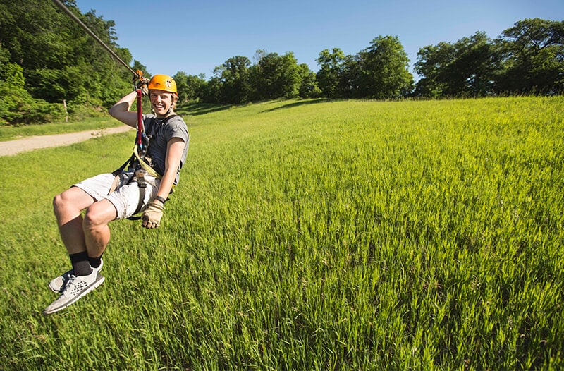 Laughing zipliner flies over lush green field