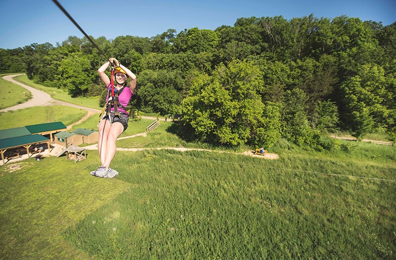 Happy girl zipliner flies over buildings and fields on the Kerfoot course