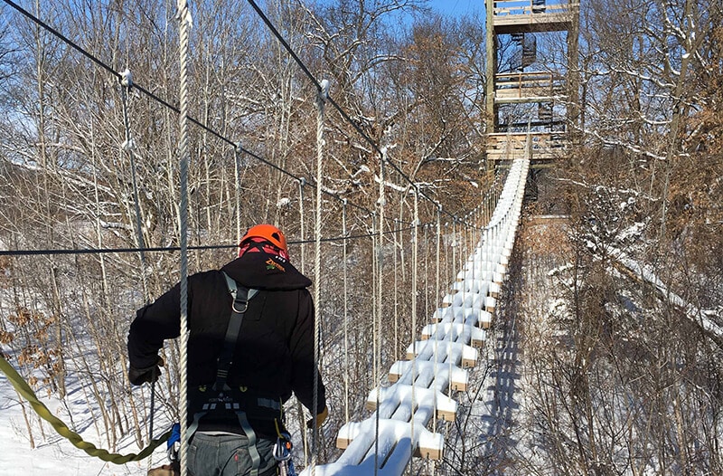 Man walks across suspension bridge with snow on it