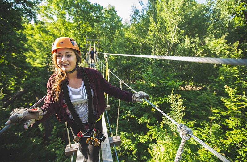 A young woman walks on a suspension bridge in a forest